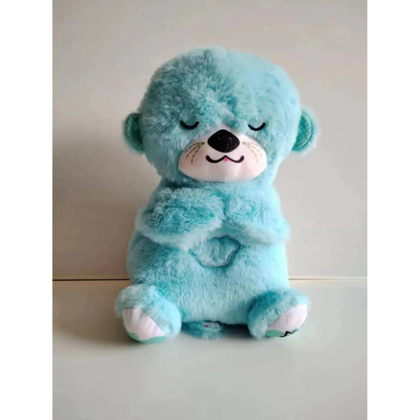 A violet plush otter sits with closed eyes and a smiling expression. This toy, designed as a sensory sleep companion for newborns, offers soothing music and lights, providing comfort on a plain background.