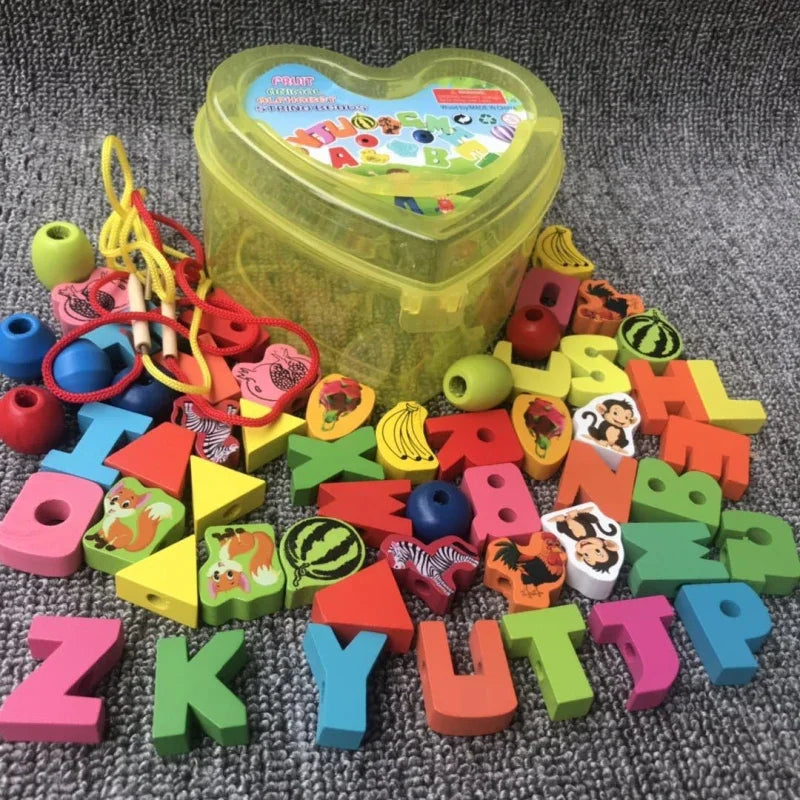 A gray surface displays colorful baby wooden lacing beads in assorted letters, fruits, animals, and geometric shapes. Ideal for enhancing fine motor skills, this 50-piece set includes a heart-shaped transparent yellow container in the background.