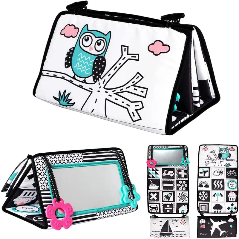 The Crinkle Cloth Book, a sensory toy for newborns 0-3 months, features an owl illustration, mirror, and high-contrast images in black, white, and teal. It includes patterns and shapes plus a pink flower-shaped teether for enhanced visual stimulation and sensory exploration during tummy time.