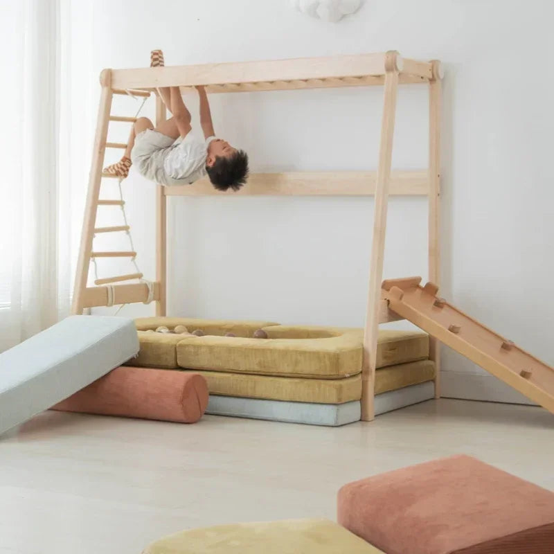 A child uses a Versatile Solid Wood Childrens Bed with Climbing Frame and Swing Features, complete with a rope ladder and slide. Soft cushions and a ball pit enhance functionality on the floor of the bright room, where light-colored decor includes a plush cloud complementing the bed.