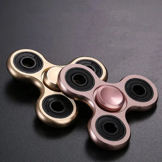 Two Premium Metal Fidget Spinners in rose gold and gold, with three rounded arms and black bearings, glimmer on a dark surface. These stress-relieving hand toys are perfect for calm moments.