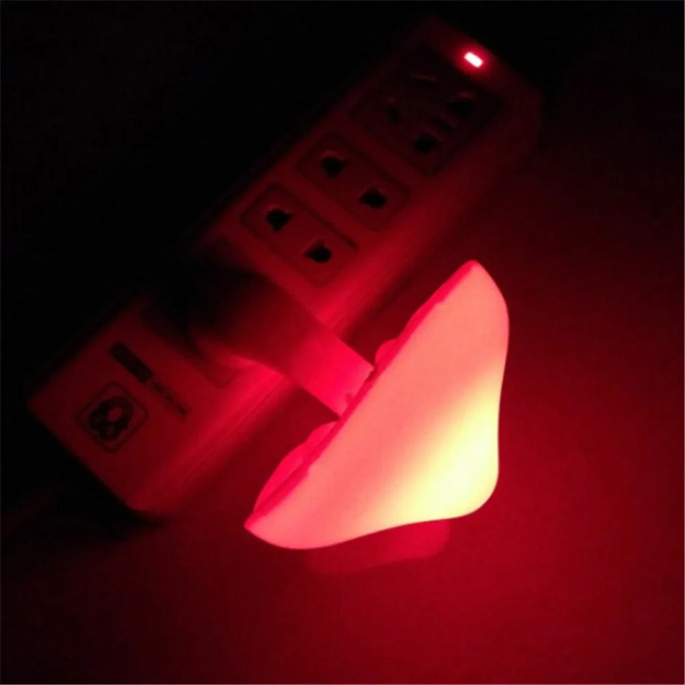 A Mushroom LED Night Light with Sensor Control in warm white is plugged into a power strip, its curved shape softly illuminating the area around it.
