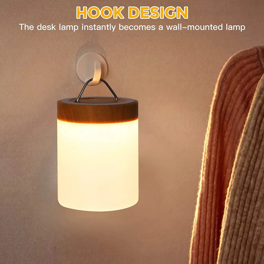 The Portable Touch-Sensitive LED Night Light, featuring a wooden top, hangs on a wall hook and emits a warm glow. Caption reads: HOOK DESIGN: Instantly become a wall-mounted lamp. A striped fabric can be seen on the right.
