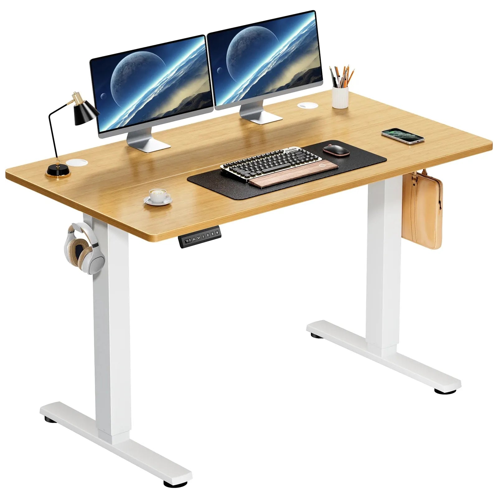 A modern bamboo JHK Electric Height Adjustable Desk features dual monitors with a space scene, keyboard and mouse on a black mat, desk lamp, coffee mug, smartphone, and stationery. Headphones hang on the side.