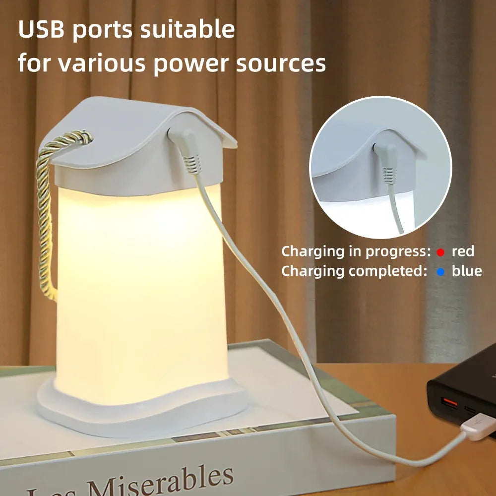 A Rechargeable Dimmable Touch LED Night Light USB Table Lamp for Bedroom Decor rests on a table beside a book, glowing warmly. Text reads: USB ports suitable for various power sources, with red and blue charging indicators, making it an ideal dimmable bedside light.