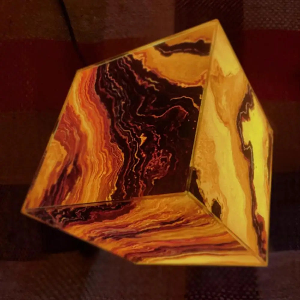 The Elegant Agate Crystal Table Lamp features a glowing, cube-shaped design with swirling black, brown, and yellow patterns reminiscent of agate crystals. It emits a warm light against a dark background, making it perfect for stylish bedroom or living room décor.
