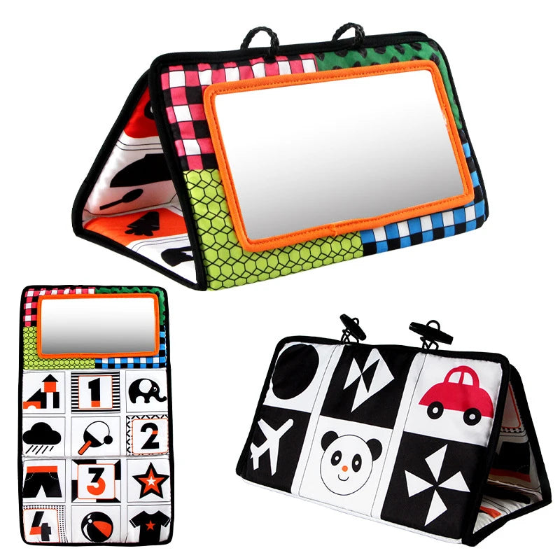 The Crinkle Cloth Book is a colorful toy for newborns aged 0–3 months, designed for sensory exploration and visual stimulation. It folds into a triangular shape with an orange-edged mirror and vibrant patterns, including images of a car, bear, airplane, and numbers.