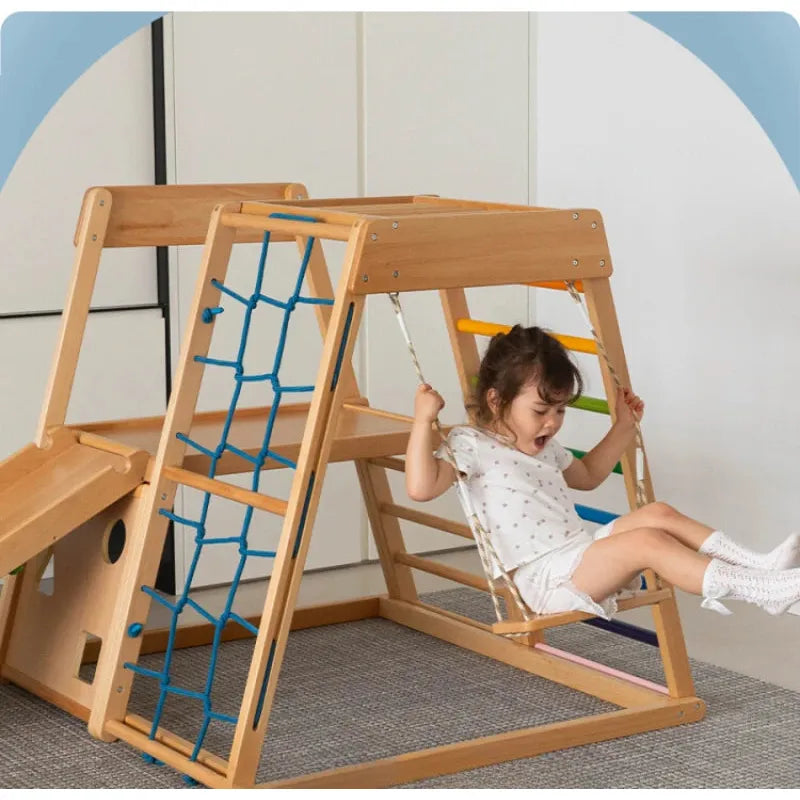A young girl in a white outfit joyfully swings on the Indoor Adventure Climbing Frame for Kids with Slide and Swing. Her legs are slightly raised in a brightly-lit room with pastel colors, perfect for fun at this indoor playground featuring a climbing net and small ladder.