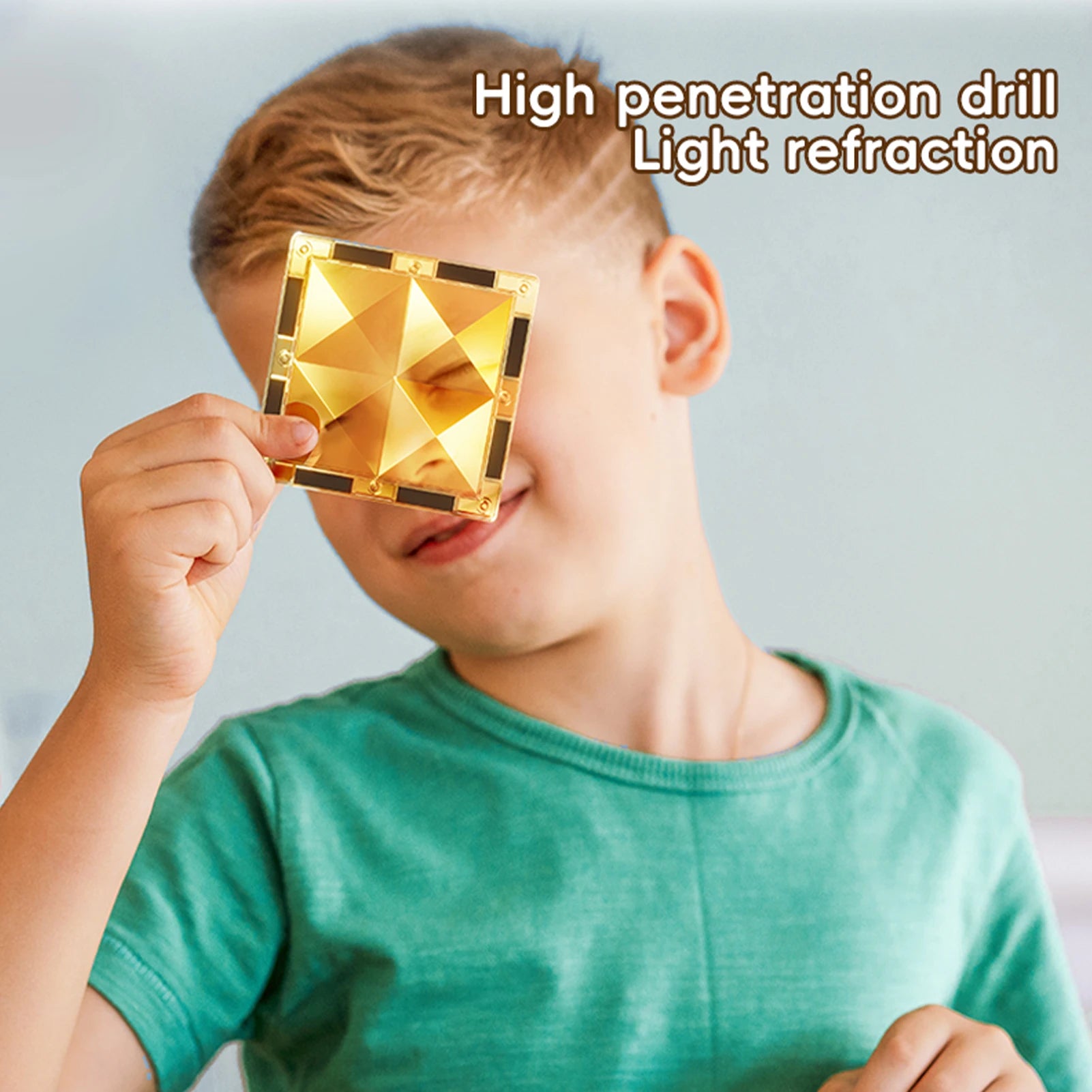 A child in a green shirt holds a reflective, gold pyramid-patterned object over one eye, exploring light refraction. Text reads Magnetic Marble Run Building Blocks Set, emphasizing the blend of curiosity and STEM-focused learning through a colorful toy for creative development.
