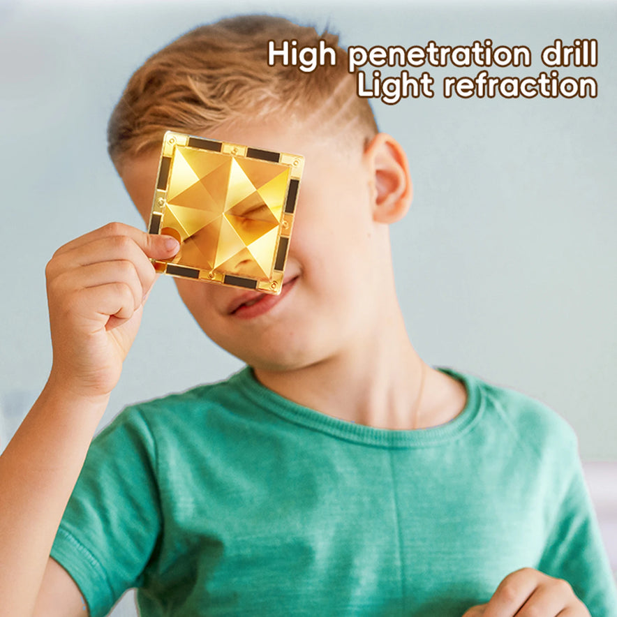 A child in a green shirt holds a reflective, gold pyramid-patterned object over one eye, exploring light refraction. Text reads Magnetic Marble Run Building Blocks Set, emphasizing the blend of curiosity and STEM-focused learning through a colorful toy for creative development.