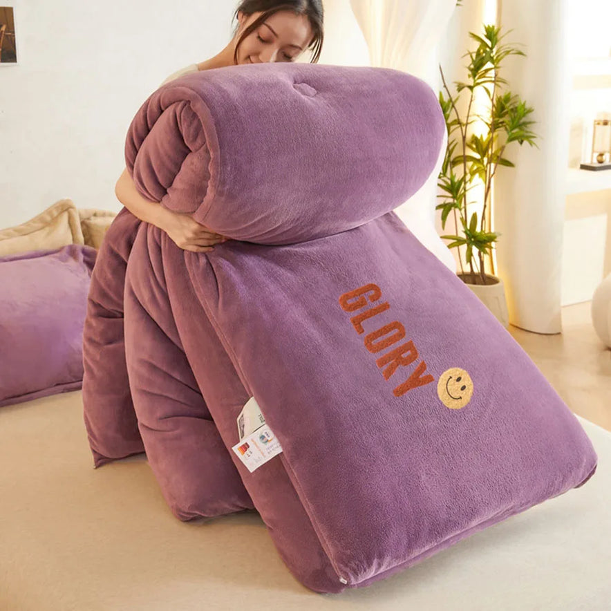 In a well-lit room with soft furnishings, someone lifts the KDJEIKZ Ultra Cozy Winter Weighted Blanket made of plush purple milk velvet, embroidered with GLORY and a smiley face. This luxurious comforter enhances coziness, making it ideal for chilly evenings.