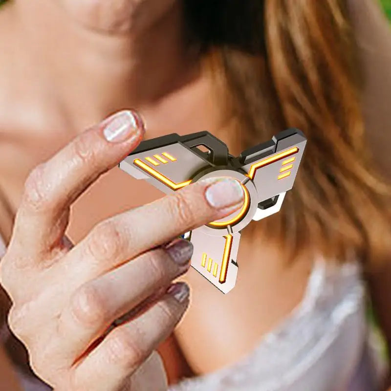 A person in a sleeveless white top holds the metallic Spinner Gyroscope Toy, showcasing its glowing orange accents that enhance focus. The blurred background emphasizes this portable, collectible fingertip toys unique design for travel play and fun.