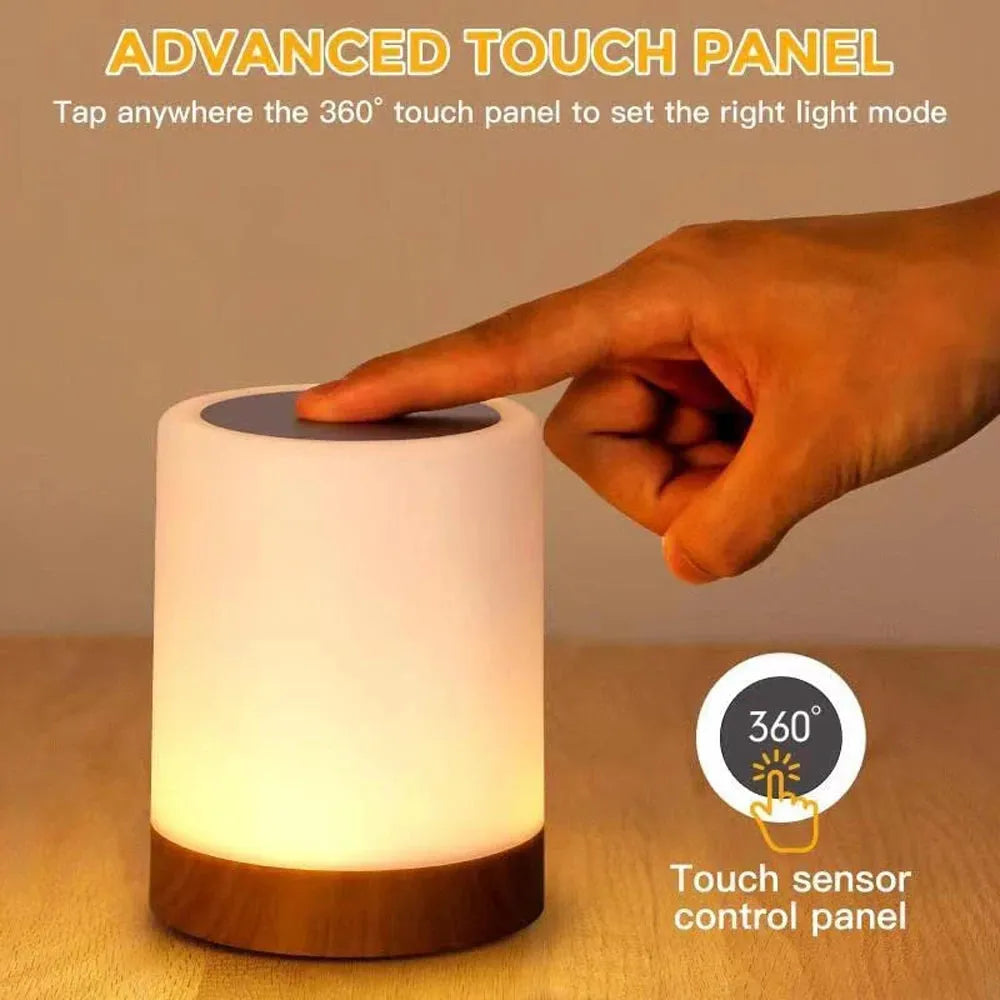 A persons hand taps the top of a cylindrical touch lamp with a wooden base. The Portable Touch-Sensitive LED Night Light glows warmly, featuring an Advanced Touch Panel and 360° touch sensor control.