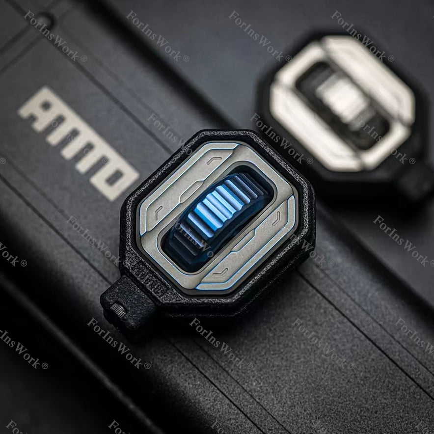 A close-up of the Ammo Cracker Unzip Roller Fidget Toy Stress Relief Slider EDC Tool in titanium blue, showcasing its mechanical, futuristic design on a black surface. A similar titanium blue slider appears blurred in the background.