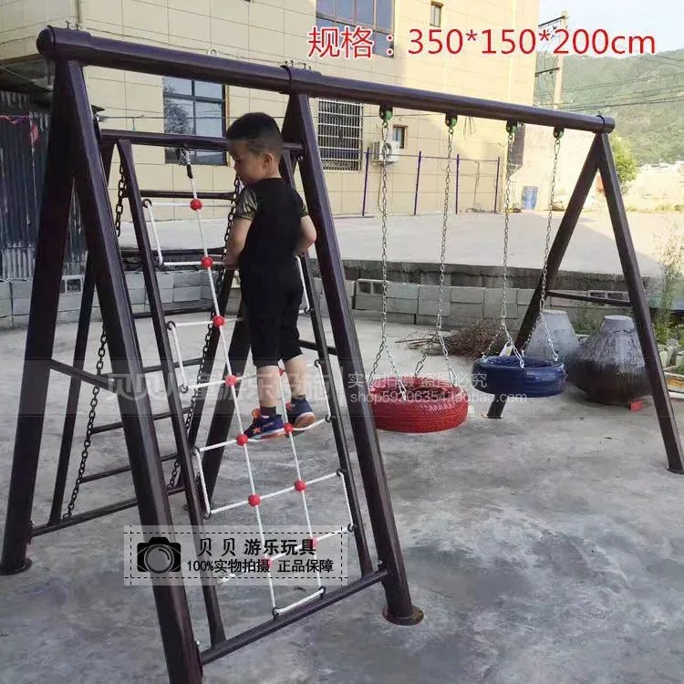 A young boy, dressed in black, climbs an Outdoor Steel Climbing Frame Swing for Childrens Sensory Integration Training. Beside him, tire swings sway gently. The play area offers fun and aids sensory integration under the clear sky.
