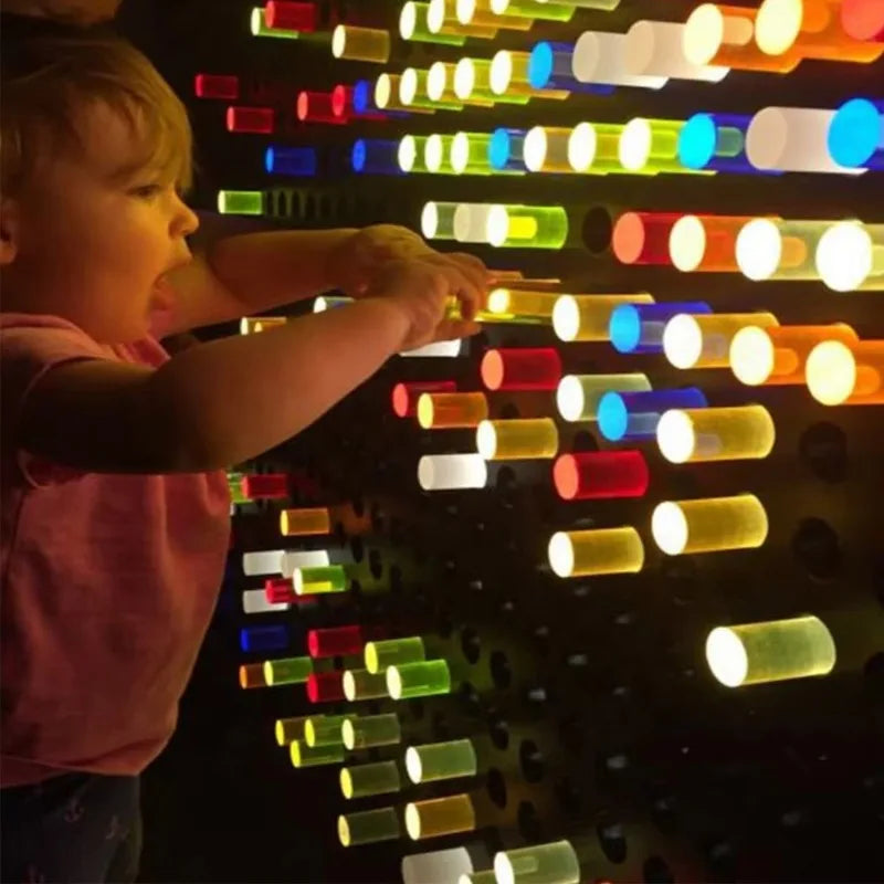 A young child excitedly plays with the High Quality Snoezelen Sensory Room Toy Light LED Acrylic Peg Board Interactive Sensory Wall Panel for Kids with Autism, inserting glowing pegs to create colorful light patterns—perfect for any sensory room.