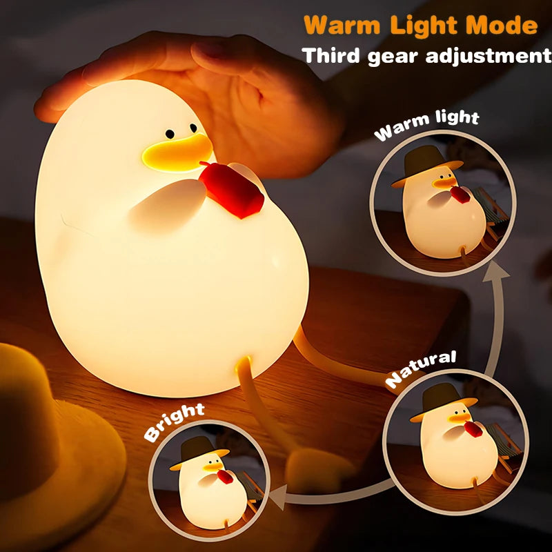 The Cute Cartoon Duck Rechargeable LED Night Light, a silicone lamp with a cartoon face and red tie, features Warm Light Mode with warm, natural, and bright settings. Its a portable night light ideal for any space, displaying each mode in circular insets beside the lamp.