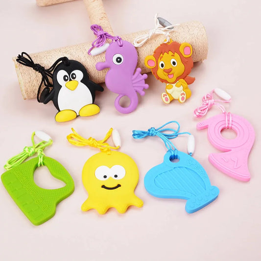 A collection of Silicone Chewable Necklaces for Kids, delightfully shaped like penguins, seahorses, and more, displayed on a light surface. These sensory teether pendants for autism and ADHD come with strings for easy handling, perfect for oral motor therapy.