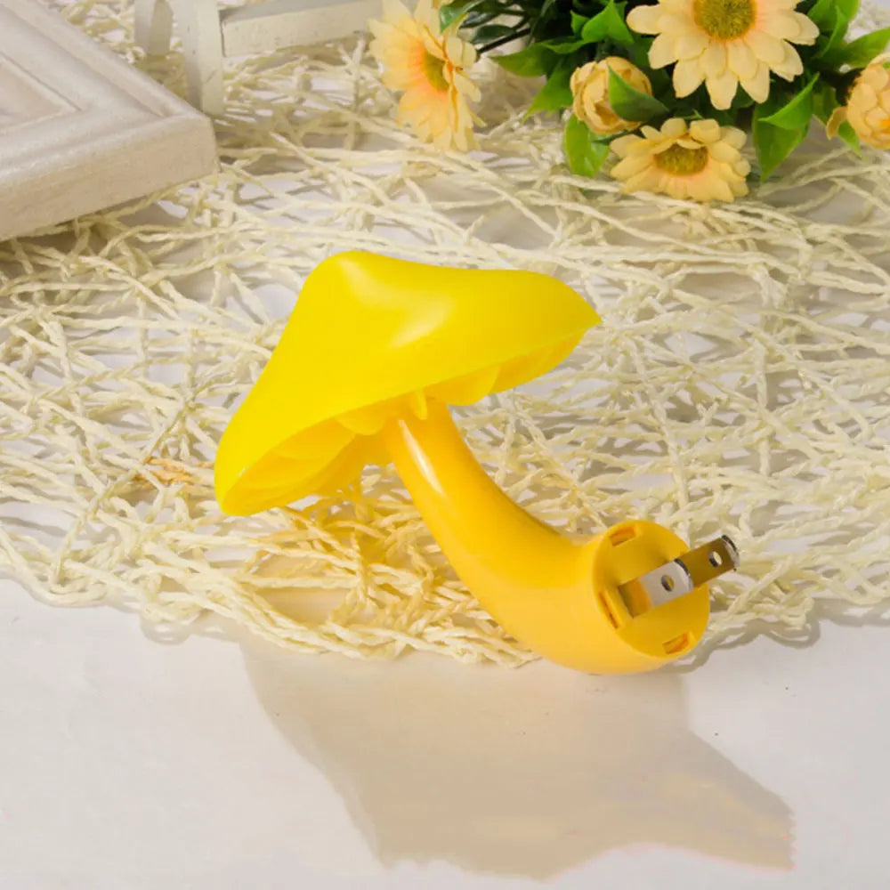 On a textured cream surface sits the Mushroom LED Night Light with Sensor Control, featuring a whimsical design with a yellow cap and stem. It provides a subtle warm white glow, accented by partially visible yellow flowers in the backdrop.