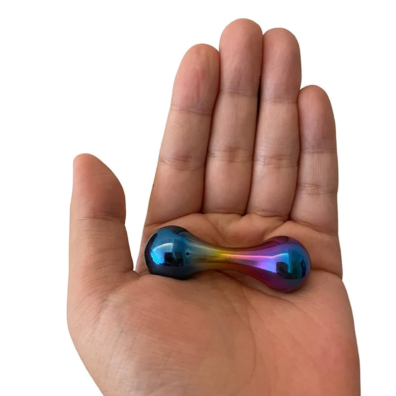 A hand holds a reflective, metallic Stainless Steel Knucklebone Fidget Tool, resembling a double-sided thimble, with hues of blue, purple, and gold designed to enhance finger dexterity and provide anxiety relief.