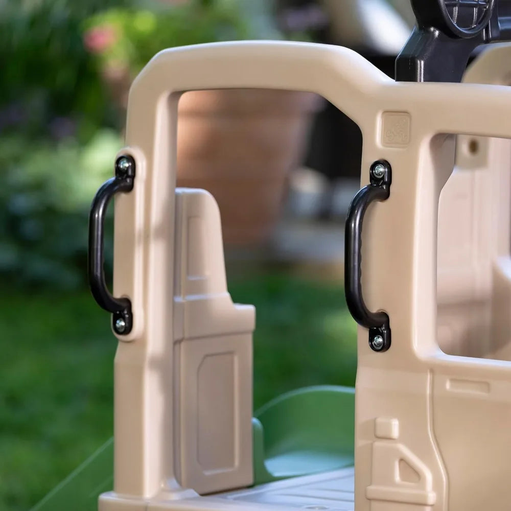 Close-up of the beige plastic Truck Climber Kids Outdoor Playset with Slide and Wall interior, featuring two black handles on the door frame. Blurred greenery in the background suggests outdoor climbing and sliding fun.