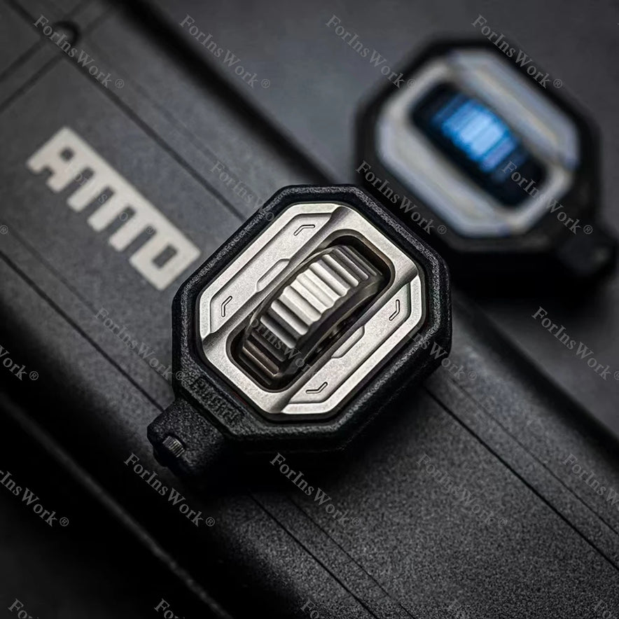 A close-up of the titanium Ammo Cracker Unzip Roller Fidget Toy Stress Relief Slider EDC Tool with a hexagonal black frame and silver center on a black surface, “AMMO” letters partially visible; another toy is blurred in the background.