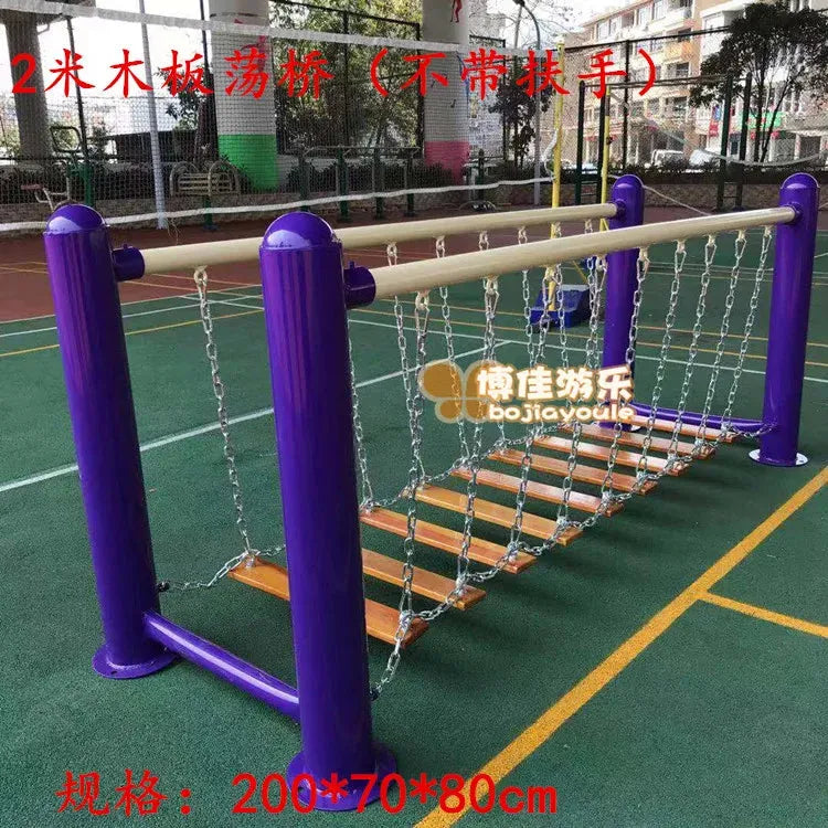 A childrens playground bridge features 2-meter wooden planks suspended by chains with purple support posts. In the background, theres a green-floored sports court and running track, perfect for unisex outdoor toys and imaginative play with swinging bridges and climbing nets for physical training.
