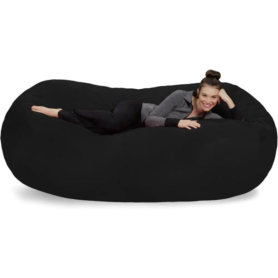 A woman with her hair in a bun, wearing dark pants and a gray sweater, lies smiling on the Bean Bag Lounger - Plush Sofas with Soft Microsuede Cover against a plain white background.
