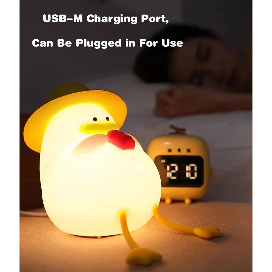 The Cute Cartoon Duck Rechargeable LED Night Light is a fun silicone bedside lamp for kids, featuring a duck with a red beak, yellow hat, and legs. Its USB-M chargeable and shown beside a clock reading 2:20 with someone sleeping in the background. Ideal gift for room decor!.