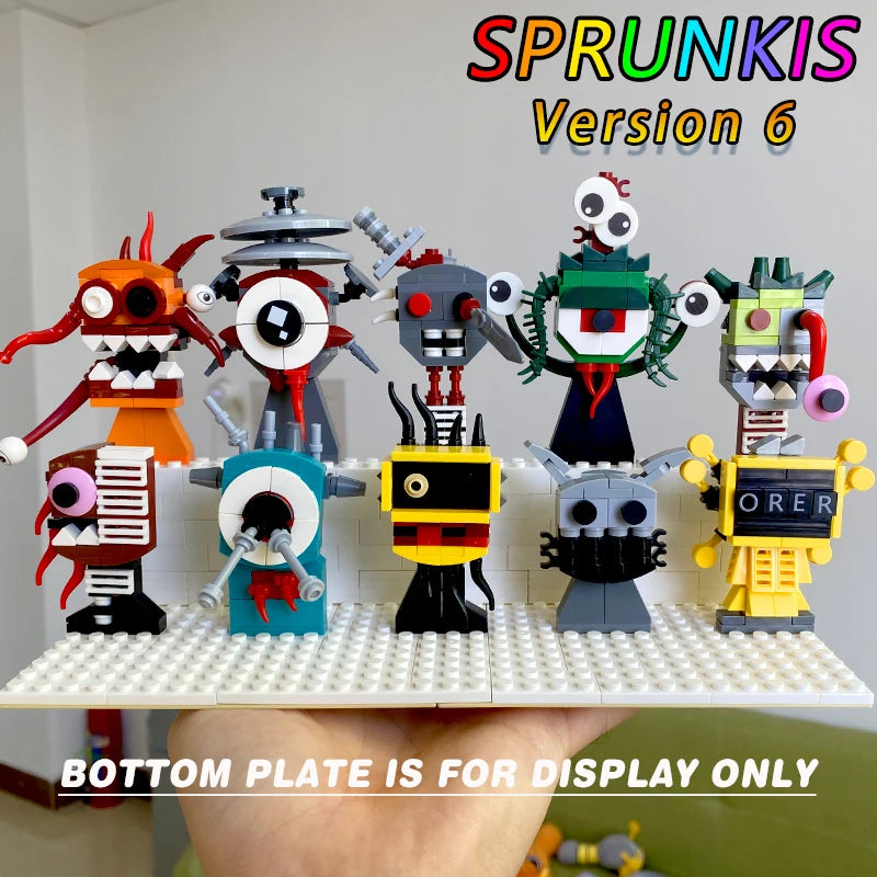 A hand holds a red baseplate featuring eight playful LEGO robots from the New Moc Incredibox Sprunki Building Blocks Set Horror Anime Music Game Bricks Toy, each with distinct faces. “BOTTOM PLATE IS FOR DISPLAY ONLY” is below.
