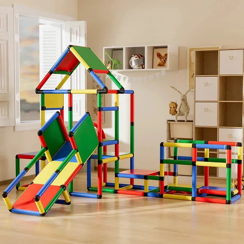 The Indoor Climbing Frame Set for Kids offers a baby slide, colorful tubes, panels, and climbing sections for adventurous play. Against light walls, it includes a cabinet and shelves in the background, perfect for sensory integration training equipment.