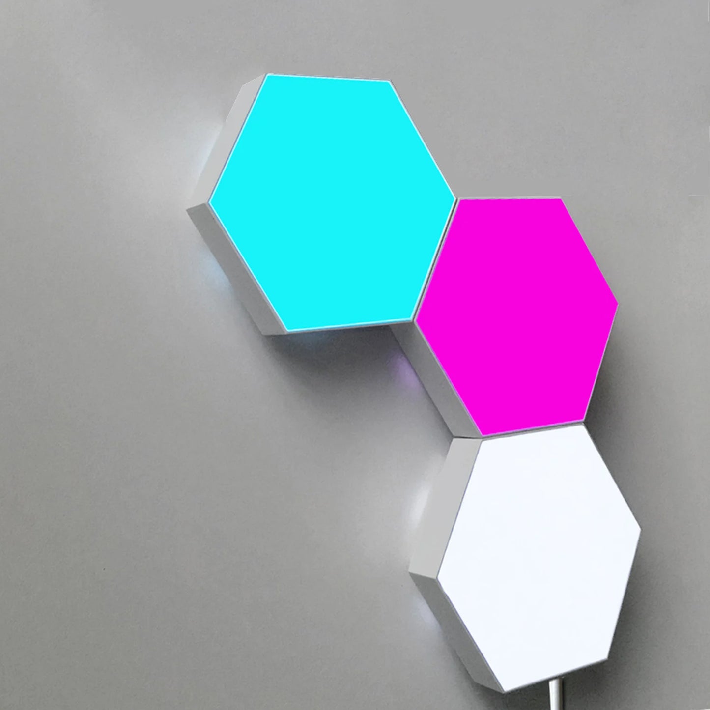 A trio of hexagonal LED wall panels on a grey wall provides a sleek look, with the top panel cyan, the middle magenta, and the bottom white. These color-changing lights are perfect for mood setting via remote control or as an innovative night light.