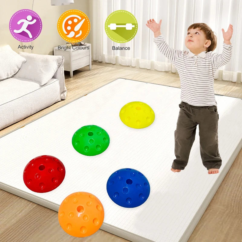 A child gleefully jumps on a soft white mat featuring five colorful dome-shaped toys in red, orange, green, yellow, and blue. The scene highlights Activity, Bright Colours, and Balance with symbols, promoting sensory play using Montessori-inspired Kids Balance Stepping Stones.