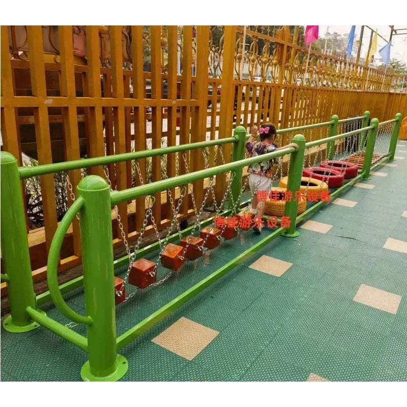 A child aged 3-8 explores a unisex outdoor swinging bridge of wooden blocks, enclosed by a wooden fence on a rubber mat. The young adventurer confidently navigates the blocks, gripping sturdy metal railings for support. This is part of an outdoor toy set for sensory and physical training fun.