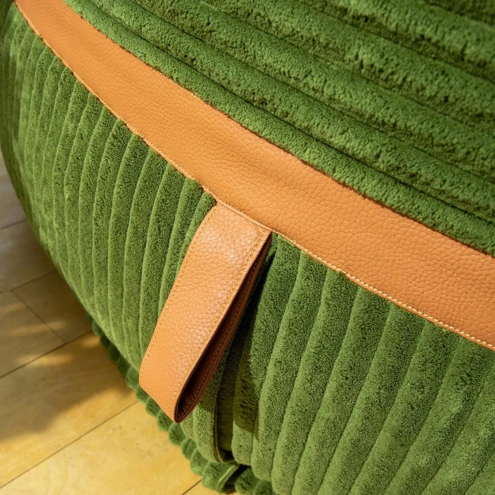 Close-up of the Fuf XXL Foam Filled Bean Bag Chair in Moss Green, 6 Feet, with a horizontal tan leather strip, removable cover, and tan leather handle, resting on a light wood floor.