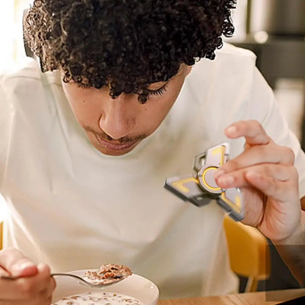 A person with curly hair is at a table, eating cereal from a bowl with a spoon while holding the Spinner Gyroscope Toy Children Spinner Fidget Toy Portable Collectible Gyro Toy Funny Fingertip Toy Travel Playing Toy to enhance focus as they concentrate on their meal.