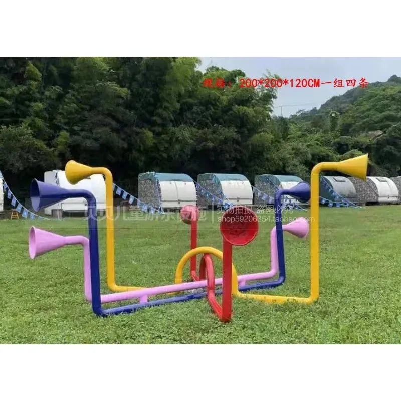 The Outdoor Steel Climbing Frame is a vibrant playground with interconnected tubes and megaphone ends in red, yellow, pink, and purple, perfect for childrens sensory integration against a backdrop of greenery and industrial bins.