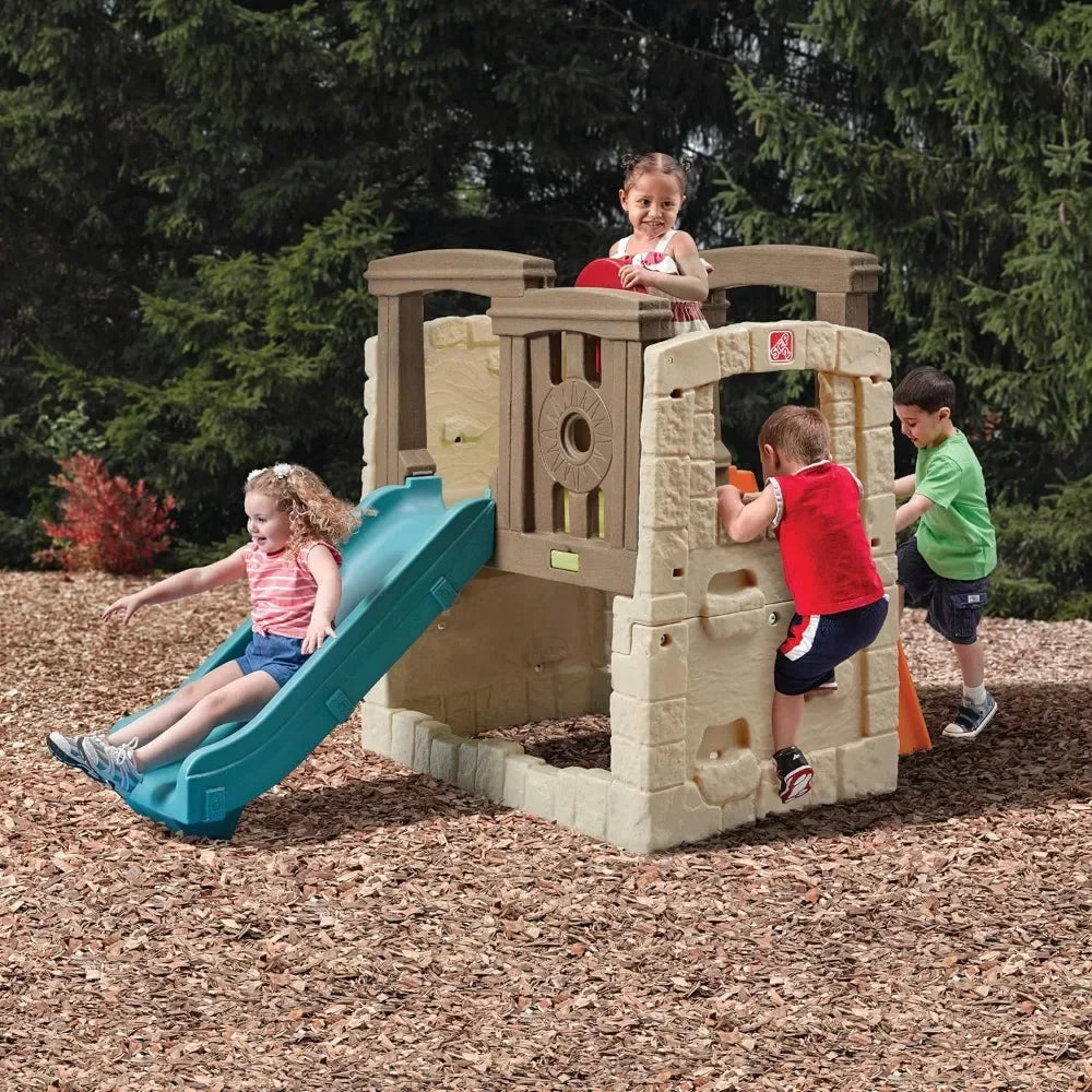 Four young children play outdoors on the Woodland Climber II Kids Playset for Ages 2 to 6 Years. One girl slides down the toddler slide, while others climb and explore, surrounded by trees and wood chips.