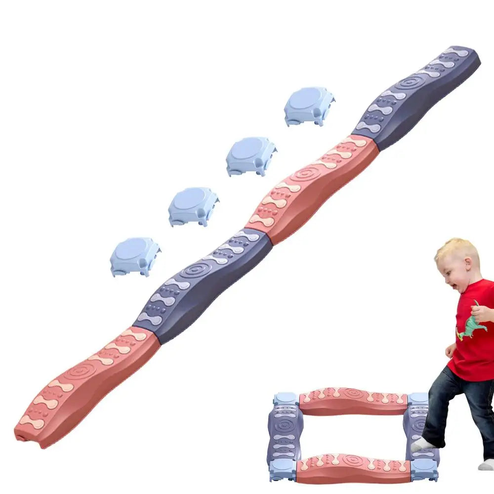A toddler in a red shirt and jeans stands beside an assembled Sensory Balance Beam Training Board for Kids in pink, blue, and black. Designed with textured grips, these colorful beams enhance coordination. Some pieces are stacked in the background for motor skills development.