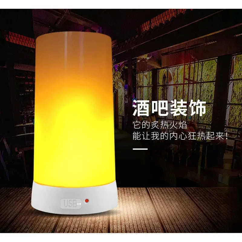 A Simulated Flame LED Night Light with a white base glows in yellow and orange on a table in a dimly lit bar setting with Chinese text. Featuring versatile use, it includes a visible USB port to power its realistic flame effect.