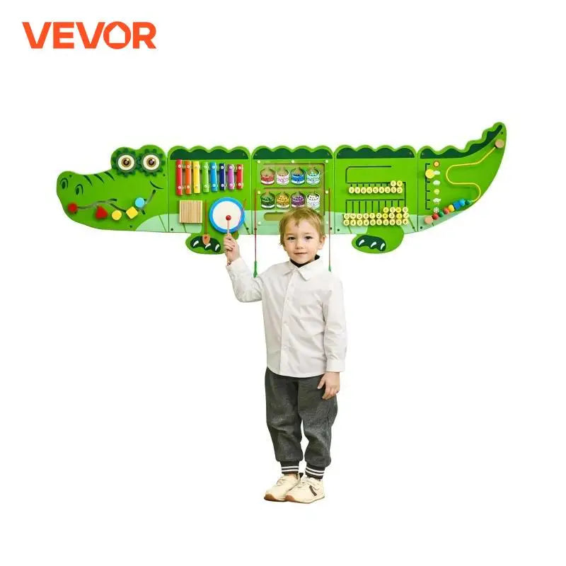 A young child stands in front of the Vevor 9 Activities Crocodile Kids Busy Hanging Board, a wall-mounted Montessori puzzle panel with colorful sensory toys that support fine motor development. The VEVOR logo appears in the top left corner.