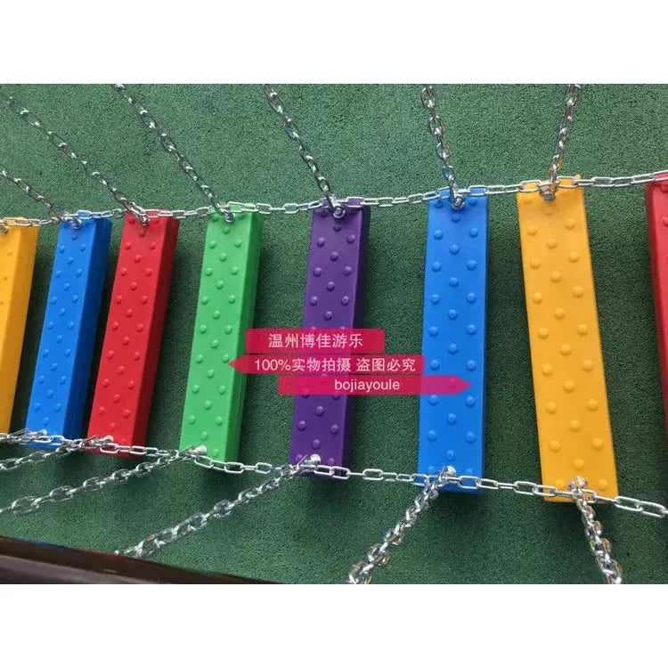 This colorful metal swinging bridge features red, yellow, green, blue, and purple rectangular stepping boards suspended by chains over a textured green surface. Ideal for unisex children aged 3-8, it showcases 100%实物拍摄 盗图必究 bojiayoule in the center.