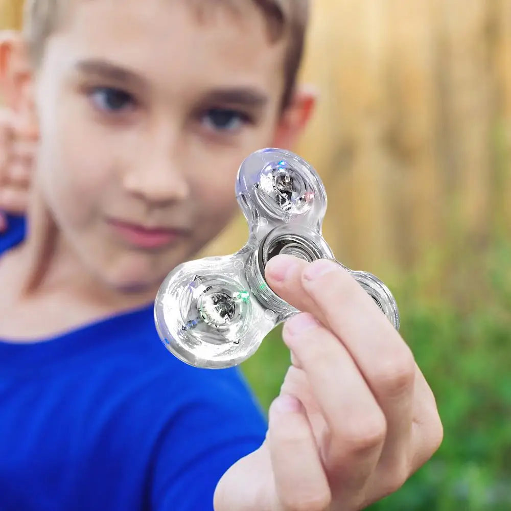 A young boy in a blue shirt focuses intently, holding out the Crystal Finger Spinners Luminous LED Light Fidget Spinner. The blurred background highlights his concentration on the glowing stress relief toy spinning in his hand.