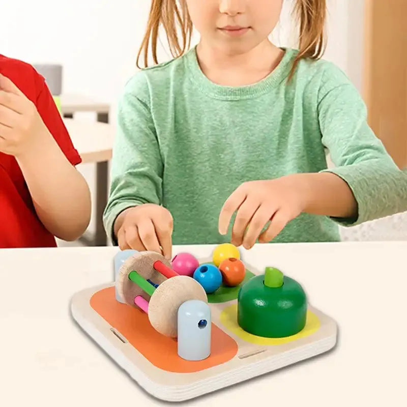 A child in a green shirt hones fine motor skills with the Interactive Wooden Sensory Learning Board, featuring shapes and pegs. Beside them, at the light-colored table, another child in a red shirt enjoys the educational fun too.