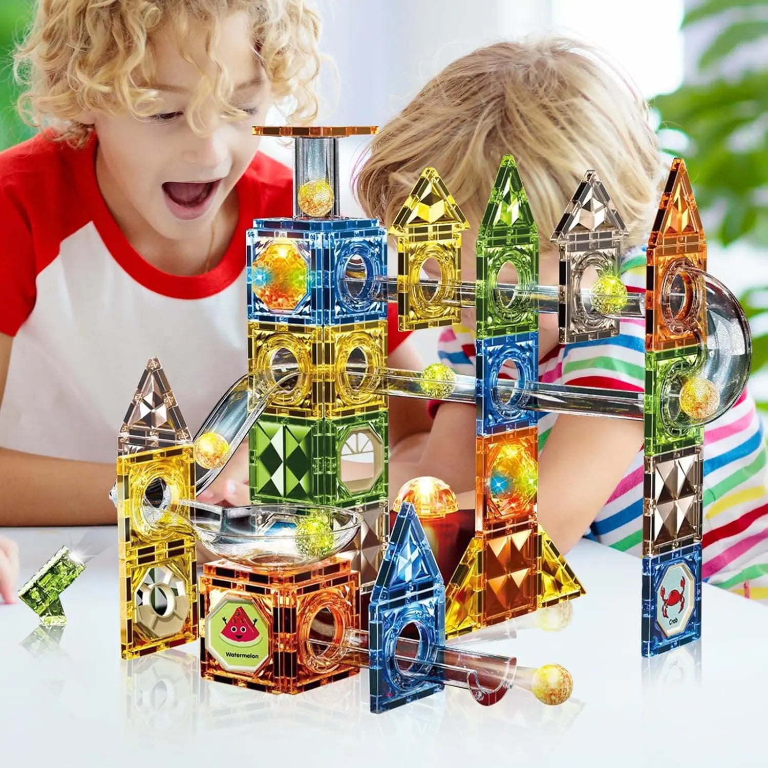 Children eagerly watch colorful balls roll in a vibrant, multi-level marble run made from the Magnetic Marble Run Building Blocks Set—an interlocking translucent tiles set in various shapes and colors, promoting STEM-focused learning and development through versatile construction.