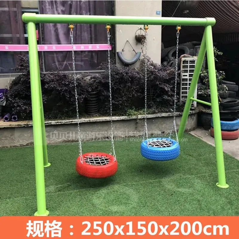 The Outdoor Steel Climbing Frame Swing, featuring two tire swings (red and blue) on a green frame set on artificial grass, offers delightful sensory integration for children. A building adorned with tires stands in the background. Dimensions: 250x150x200 cm.