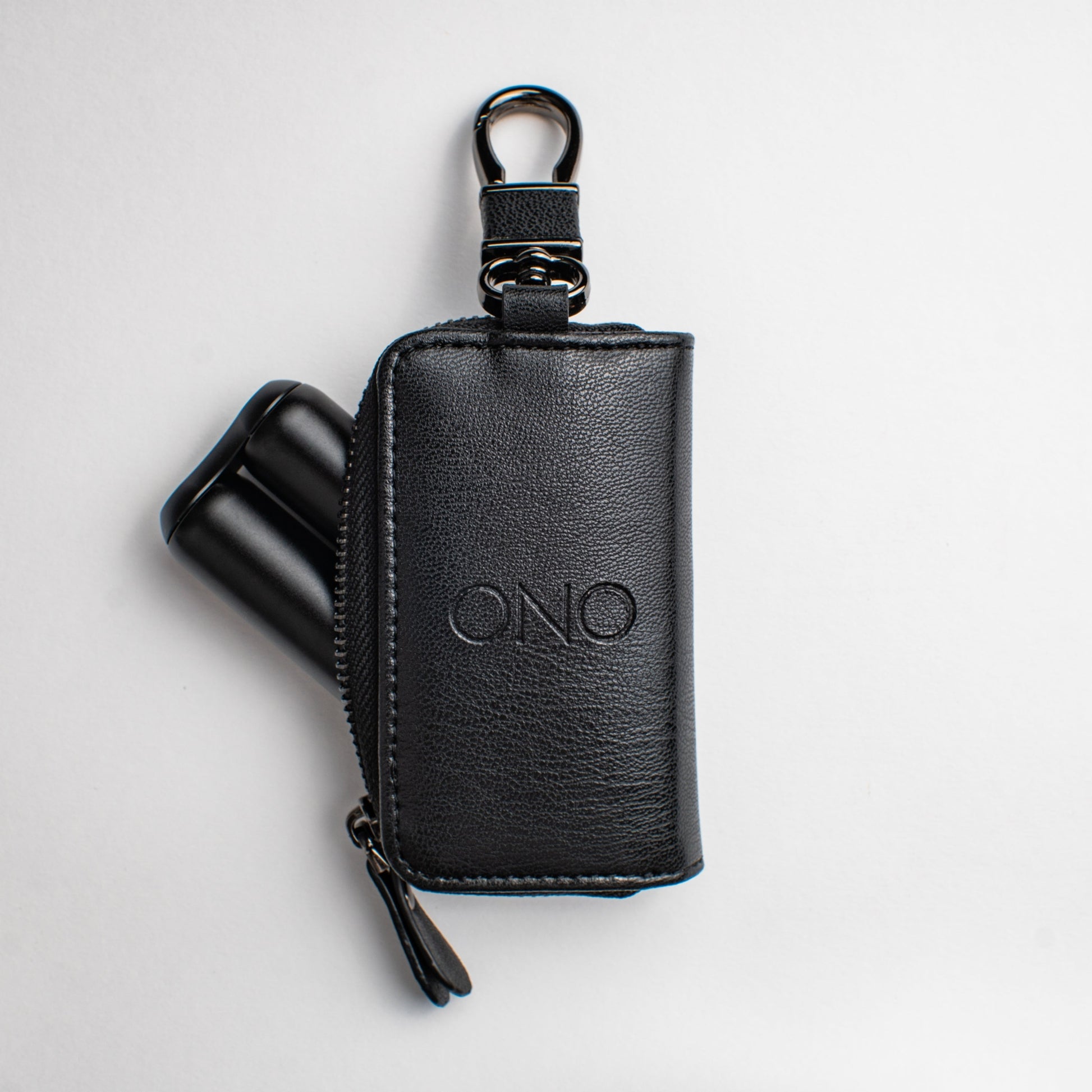 The ONO Roller Premium Keychain Case is a black pouch with an embossed ONO logo, metal top clip, and a zipper. Two black cylindrical ONO tools are partially visible inside. The case is photographed against a white background.