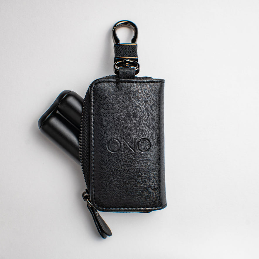The ONO Roller Premium Keychain Case is a black pouch with an embossed ONO logo, metal top clip, and a zipper. Two black cylindrical ONO tools are partially visible inside. The case is photographed against a white background.