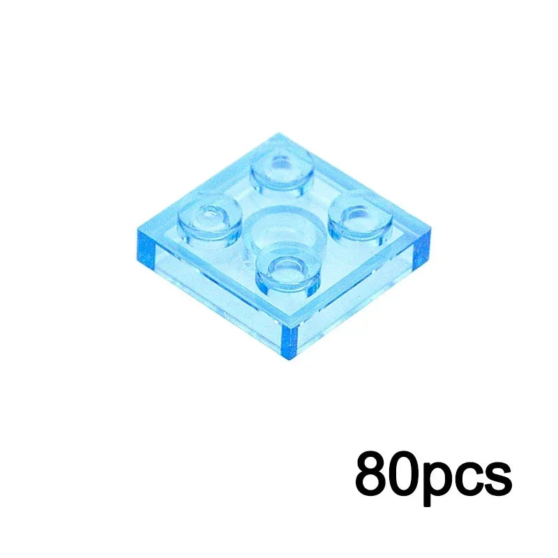 A 2x2 TRN light blue square brick from the MOC Transparent Bulk Brick Set, compatible with Lego, is displayed on a white background. The set includes various sizes—perfect for building collections. 80pcs appears in black in the lower right corner.