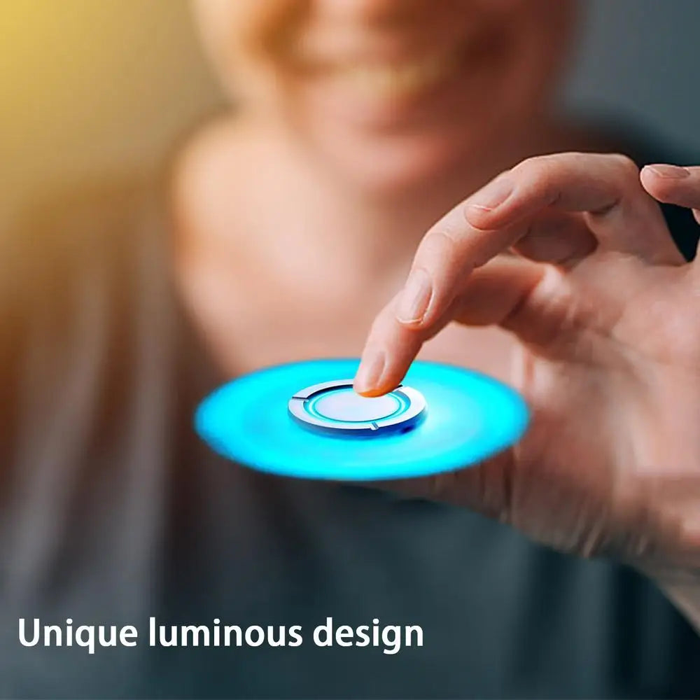 A person holds a glowing blue Spinner Gyroscope Toy Children Spinner Fidget Toy between their fingers. The blurred background highlights the spinners luminous design, with text stating Unique luminous design.